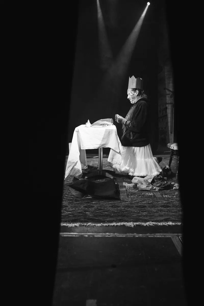 Gemaskerde performer aan een tafel in een spotlight, zwart-wit