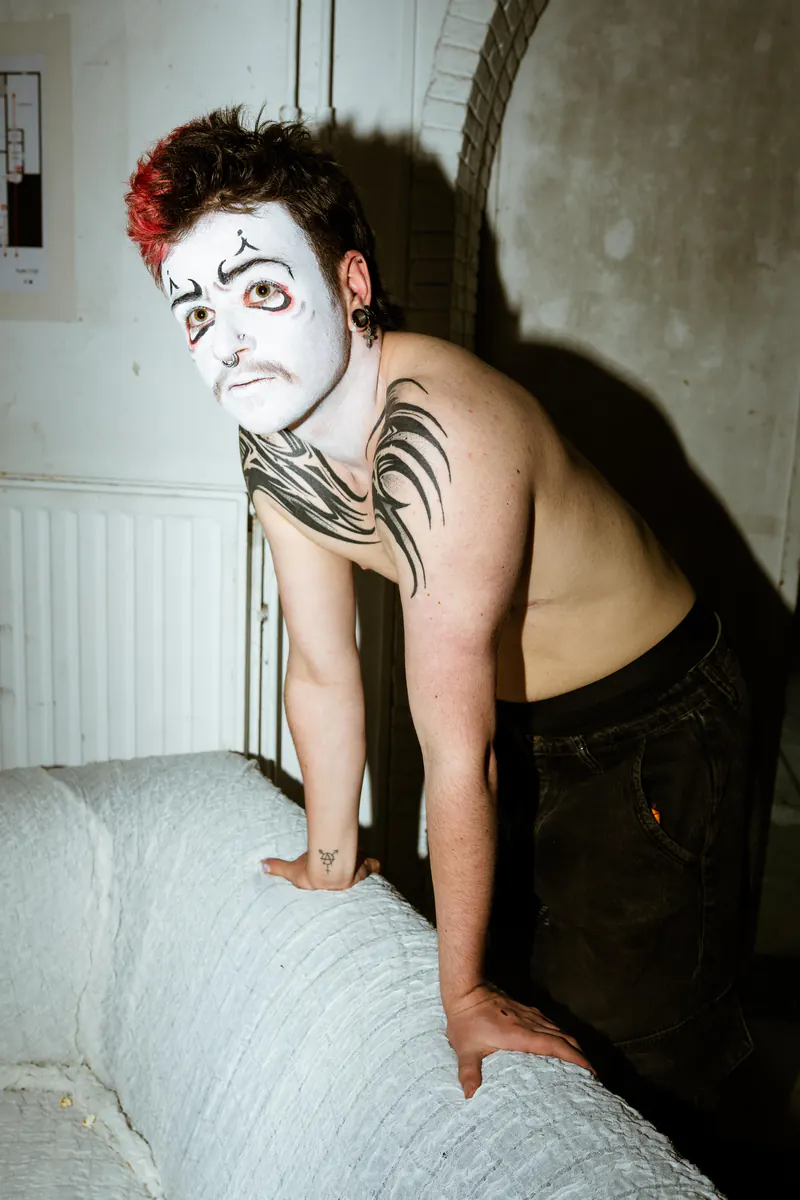 Performer in witte clownsschmink, leunend op een bed
